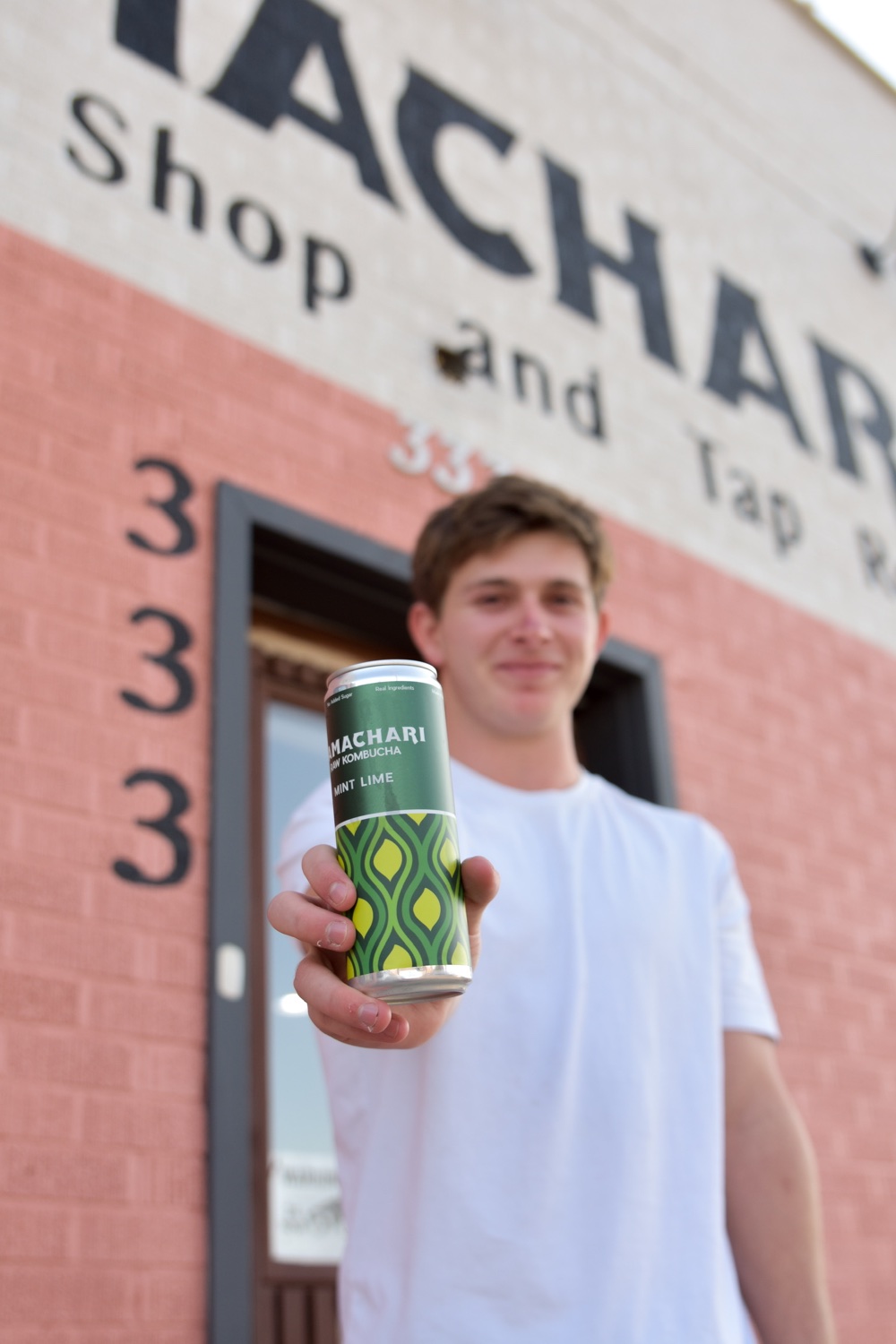 A Mamachari kombucha can held in front of the Mamachari storefront